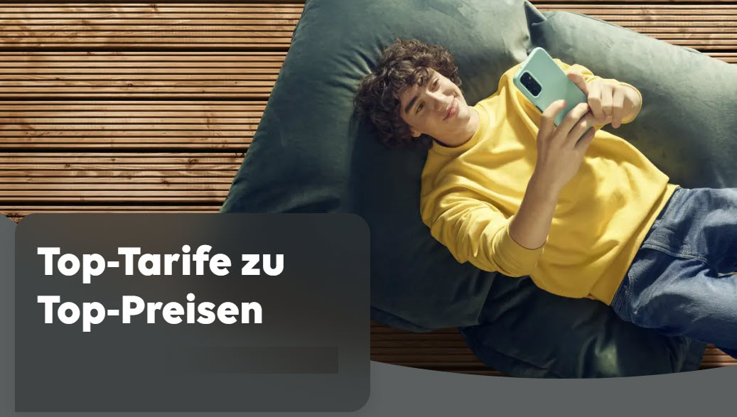 Dekoratives Bild. Ein junger Mann liegt auf einem bequemen Bodenkissen und schaut freudig auf sein Handy in der Hand. Im Hintergrund ein brauner Holzfußboden.
