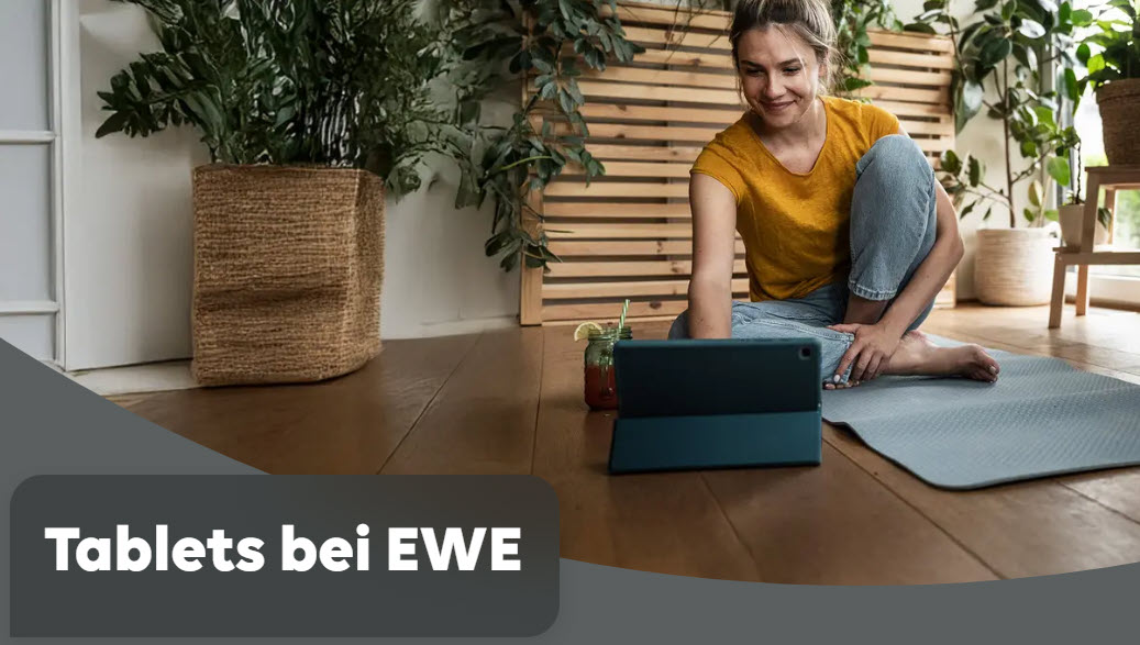 Dekoratives Bild. Eine junge Frau sitzt auf einer Yogamatte, vor ihr steht ein Tablet. Im Hintergrund grüne Zimmerplfanzen.
